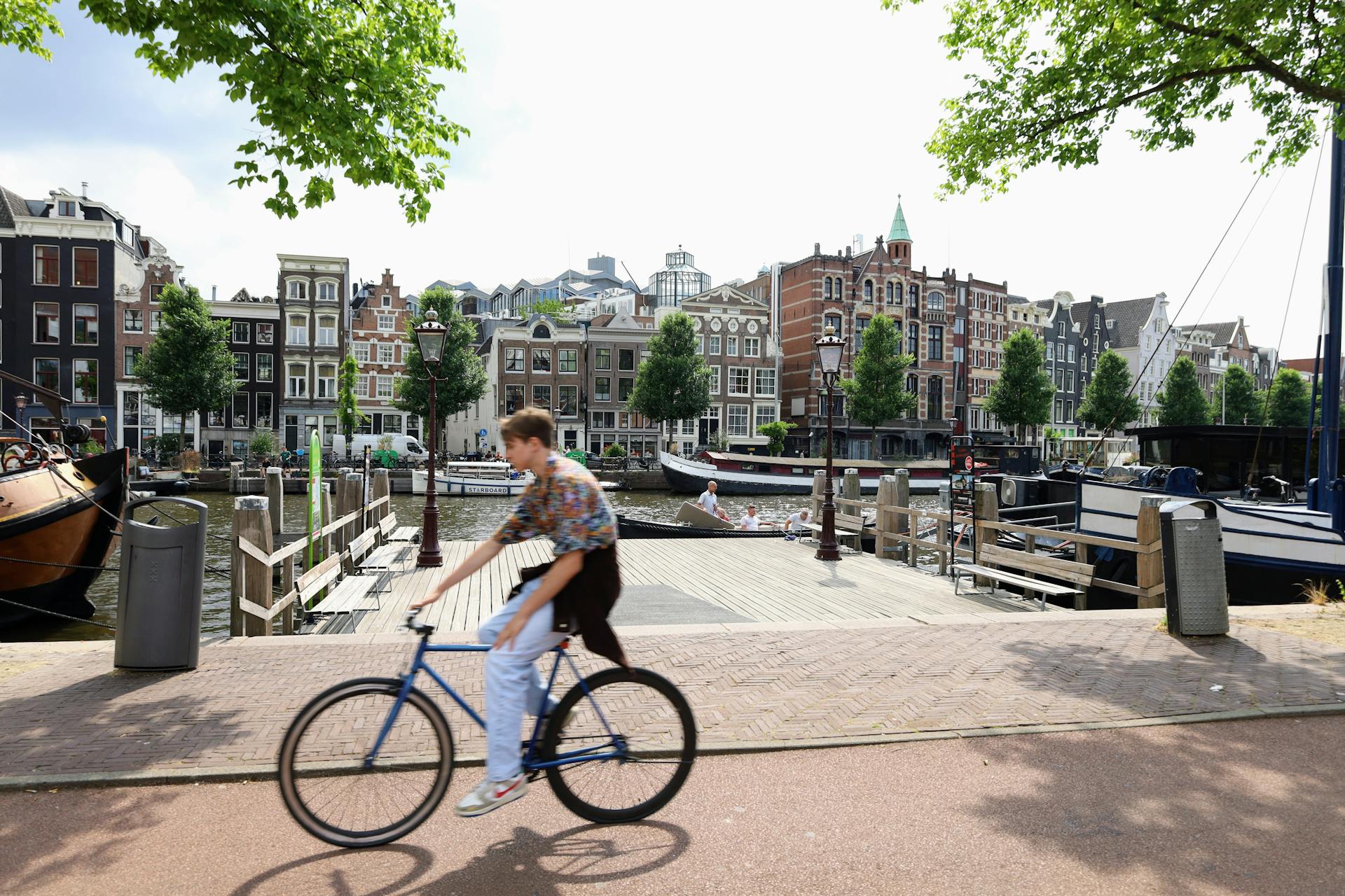 Blurred cyclist passes by picturesque Amsterdam canal with historic buildings in summer.