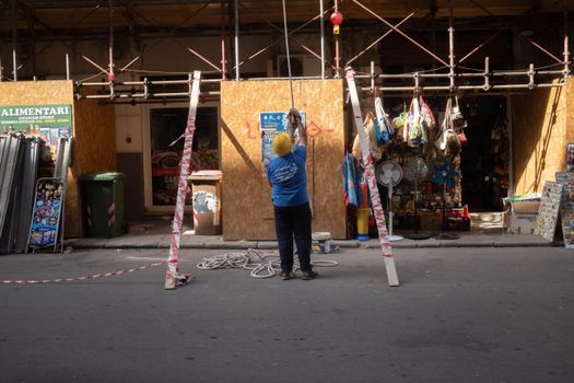 A construction worker standing on a street setting up scaffolding outside an urban storefront.