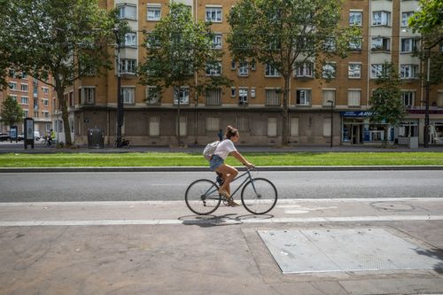 Free Woman cycling on an urban street bike lane beside a row of buildings. Stock Photo