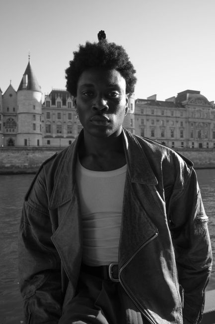 Black and white portrait of a man in a jacket by a historical building.