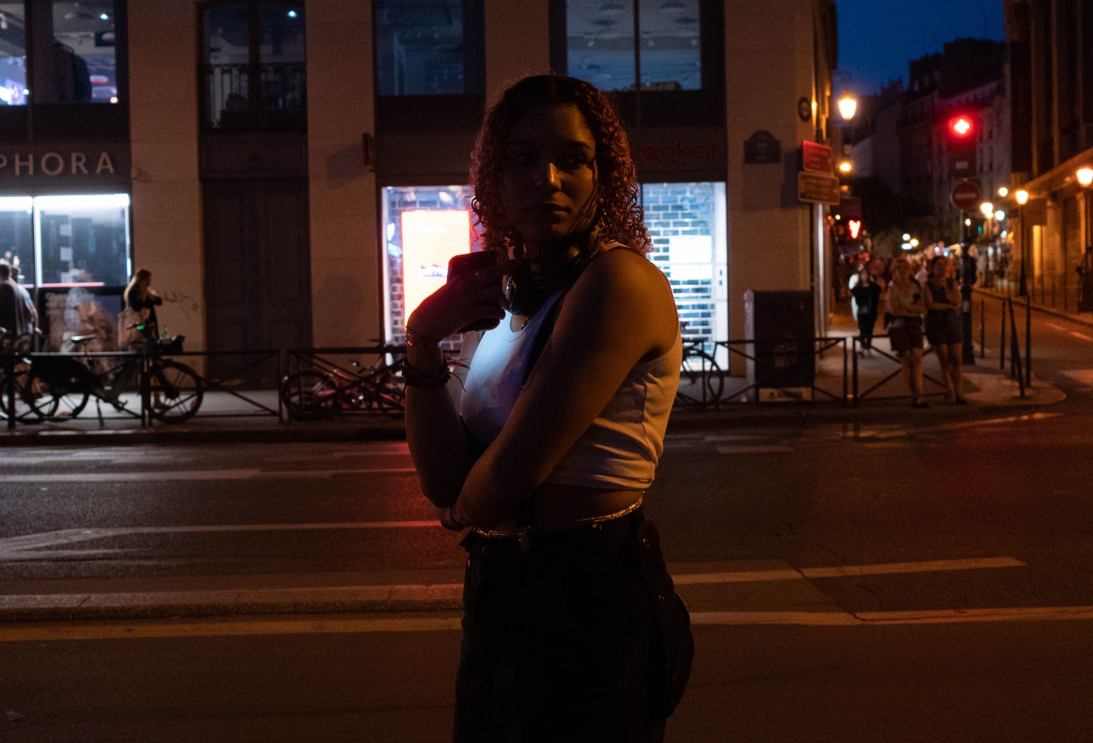 Person wearing headphones standing alone in a crowded, neon-lit city street