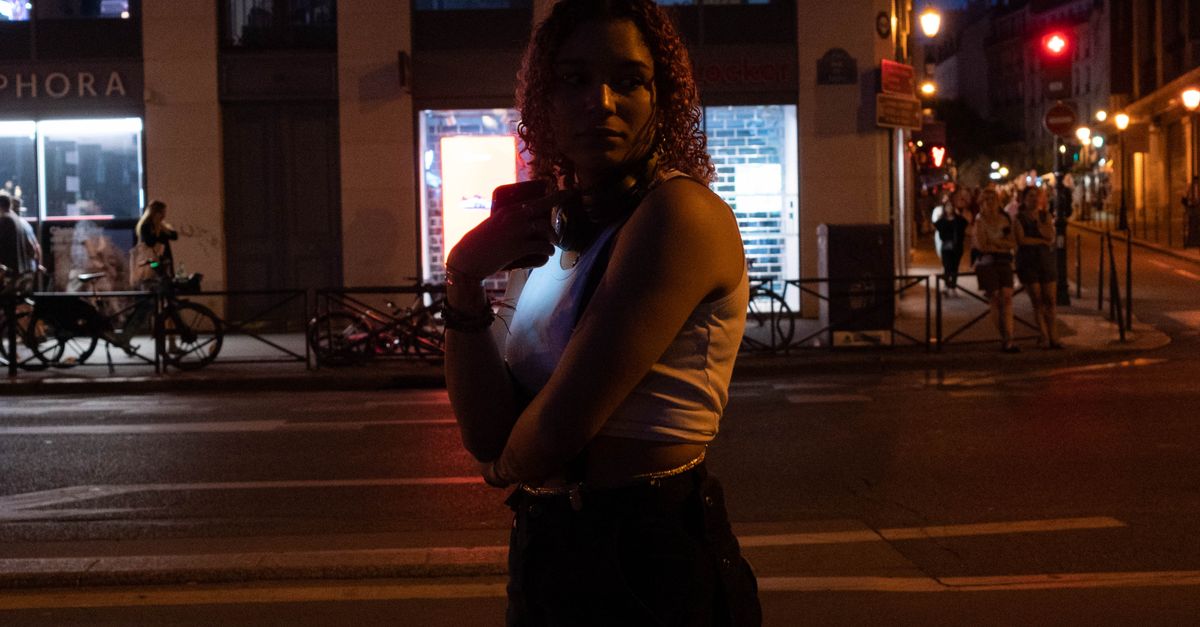 Person wearing headphones standing alone in a crowded, neon-lit city street
