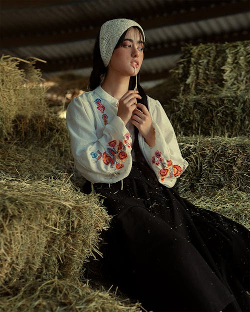 Woman in Traditional Clothing Sitting on Hay Bales