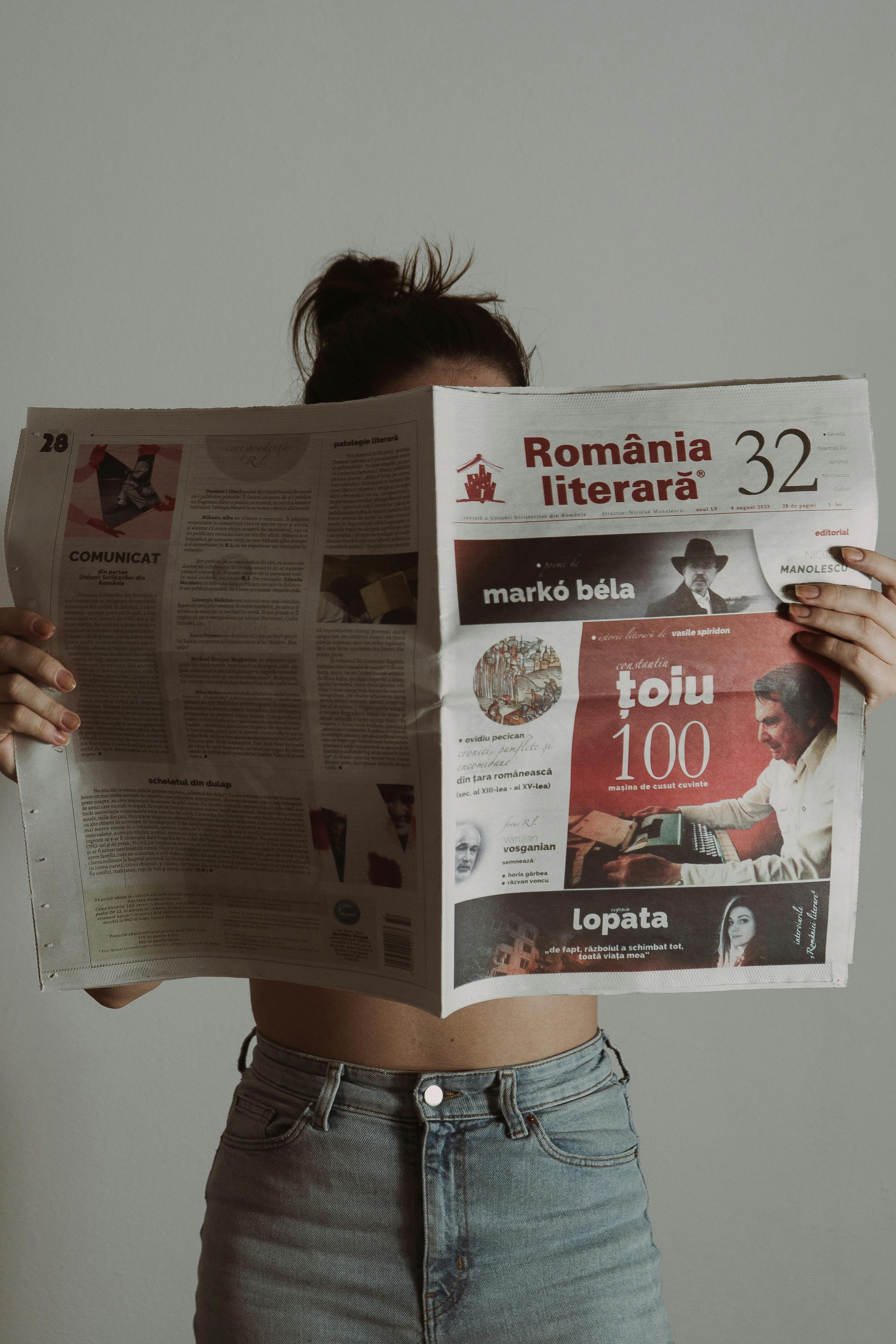 Young woman in jeans reading a Romanian literary magazine indoors.
