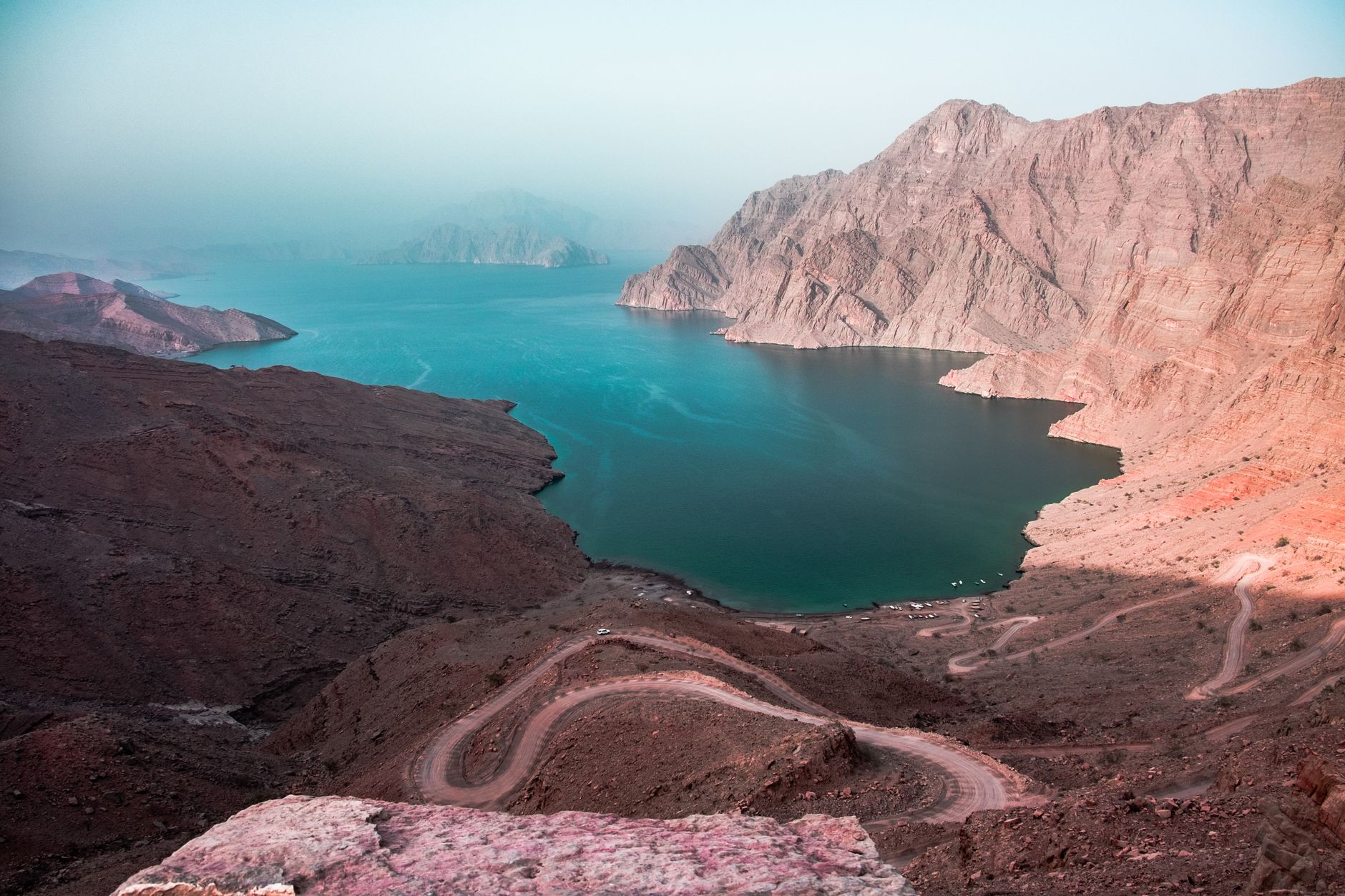 A breathtaking view of steep mountains meeting the sea, with winding roads in an arid landscape.