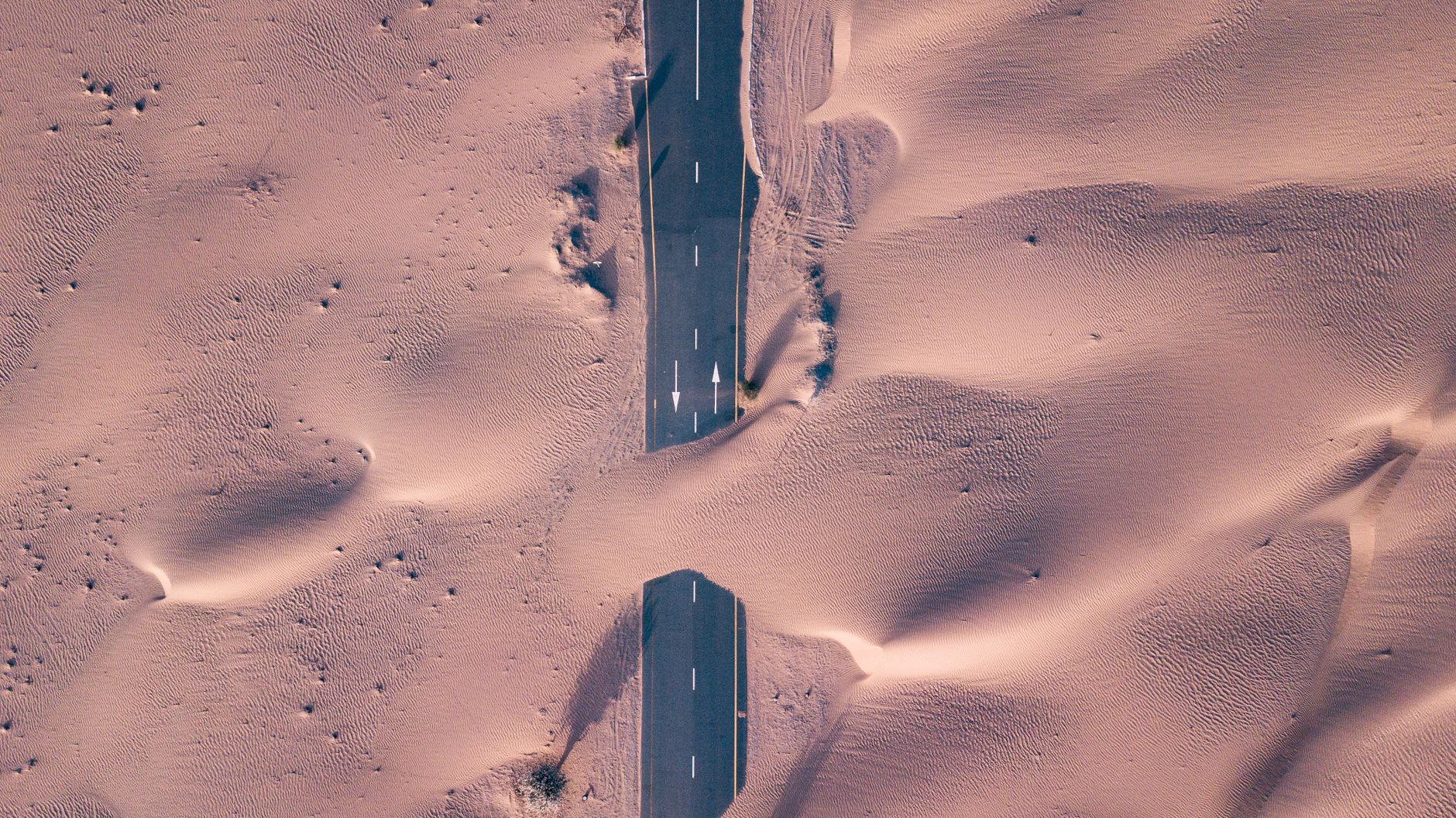 A stunning aerial photo of a road cutting through expansive desert dunes, showcasing isolation and wilderness.