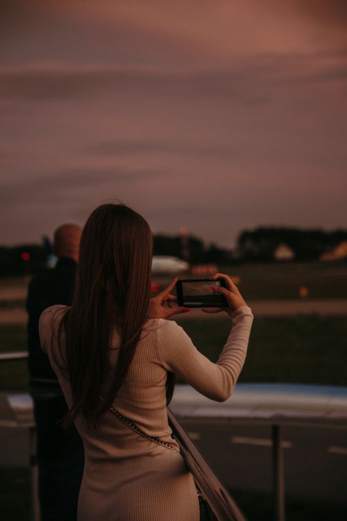 Free A woman standing and taking a picture with a smartphone during a picturesque sunset outdoors. Stock Photo
