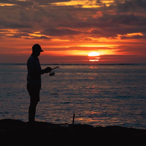 Standing on Beach Man Holding Fishing Rod at Sunset