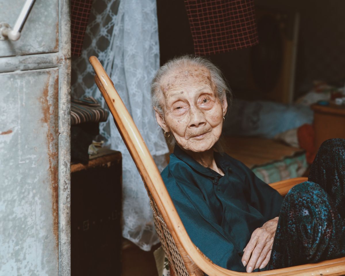 Elderly Malaysian woman seated calmly at home where oxygen equipment has been set up