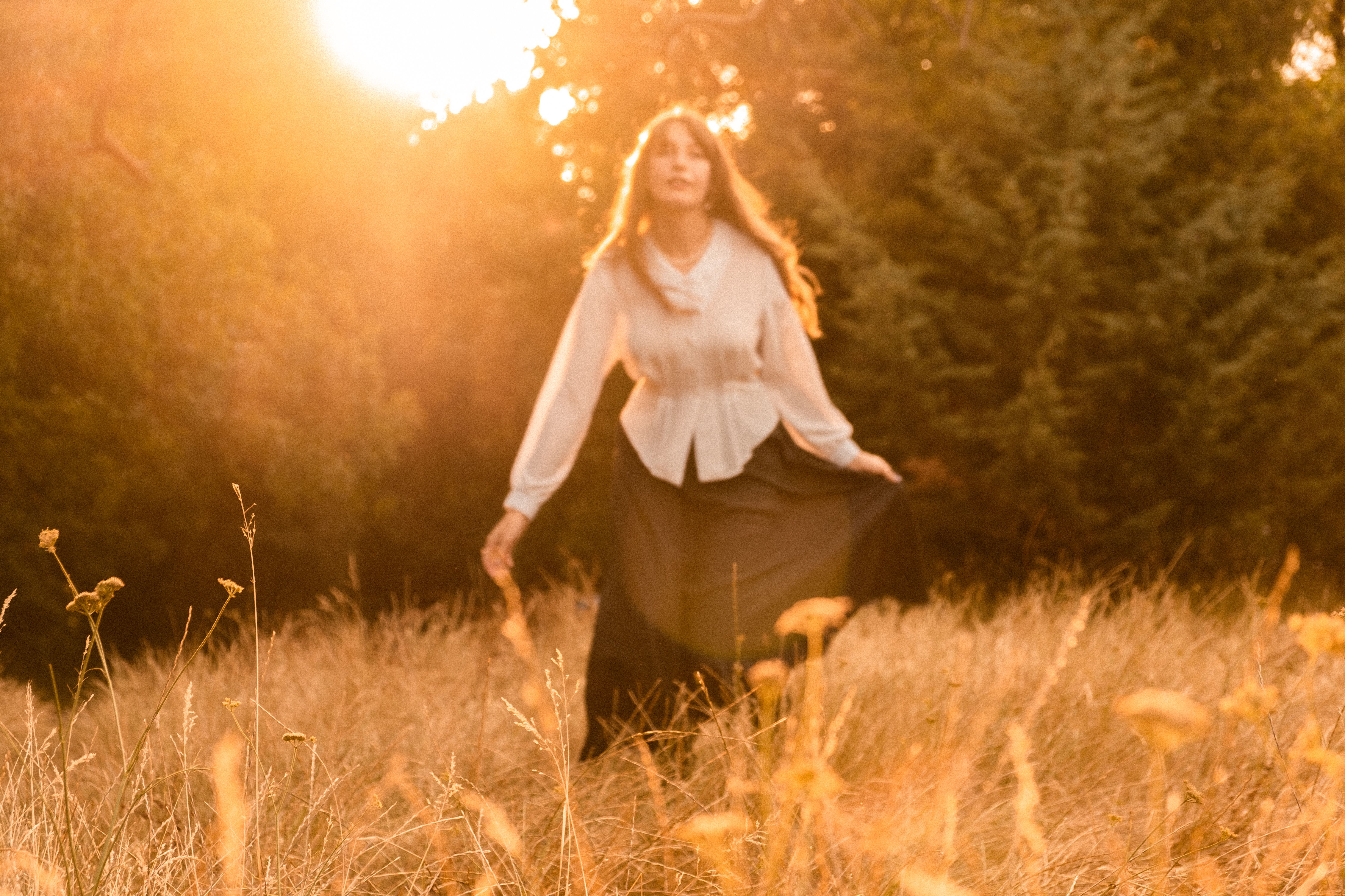 A woman in a flowing dress stands in a sunlit field during golden hour.