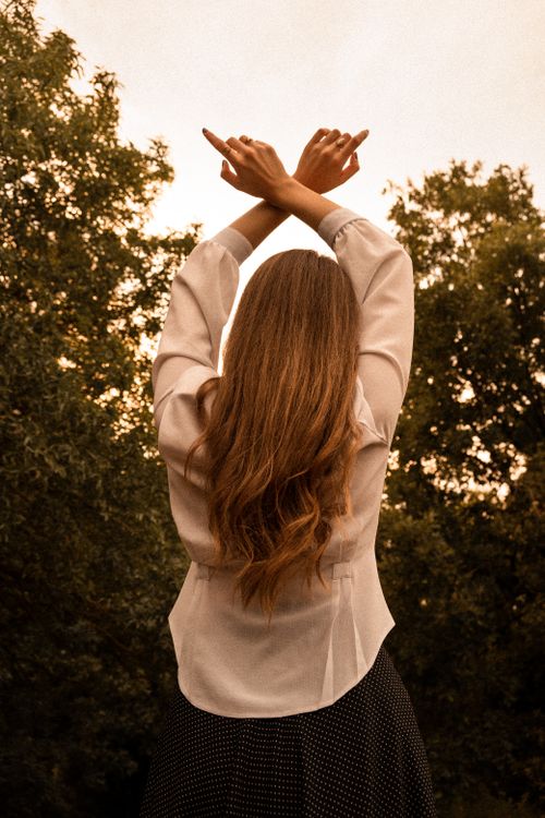 Free Woman in white shirt standing outdoors with arms raised in a peaceful setting. Stock Photo