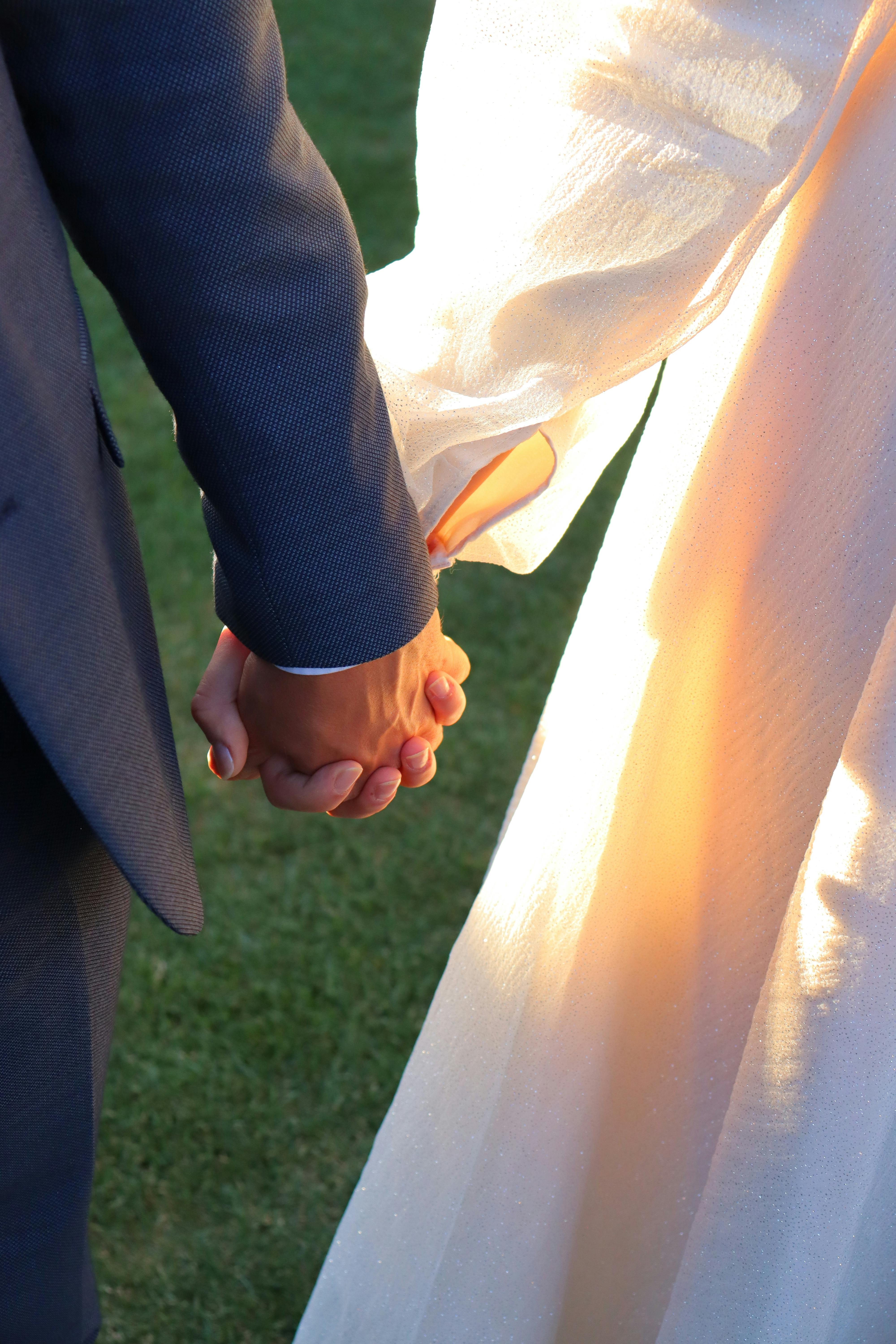 A romantic close-up shot of a couple holding hands during an outdoor wedding ceremony.