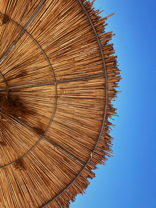 Free Close-up of a straw beach umbrella with a vibrant blue sky background, perfect for summer themes. Stock Photo