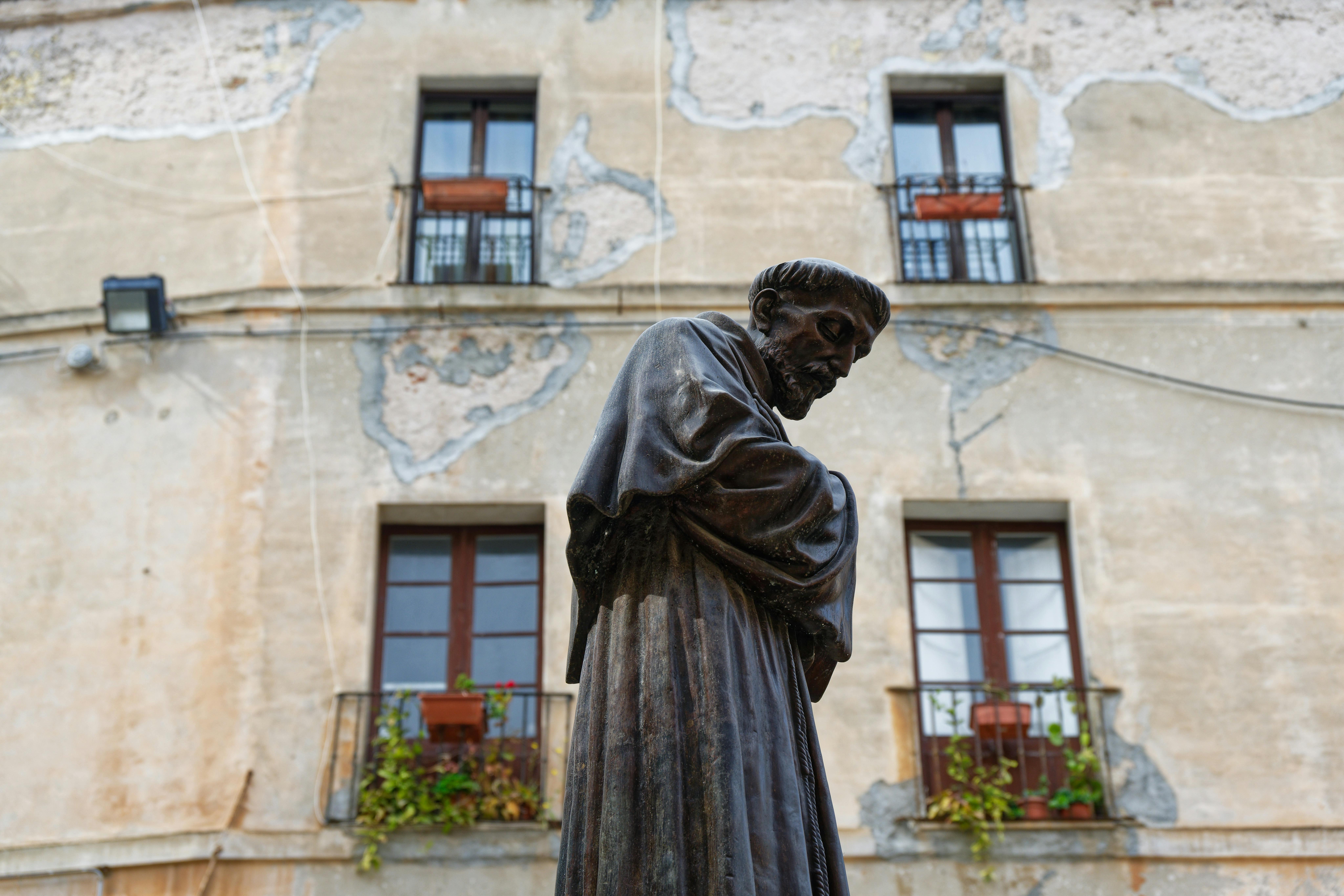 Statue of a religious figure in Cagliari, Italy with rustic building background.