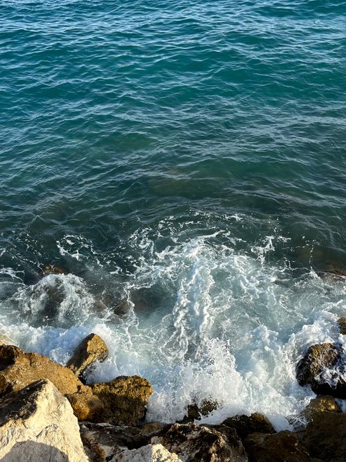 Free Dynamic ocean waves splashing against rugged coastline rocks under a clear blue sky. Stock Photo