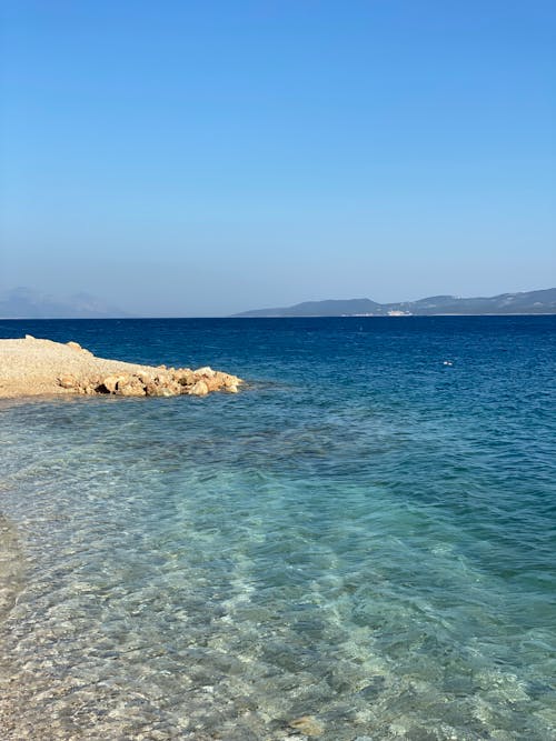 View of Clear Turquoise Water and Hills in Distance under a Blue Sky 