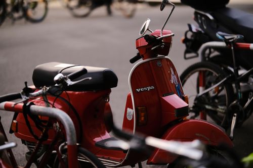 Free A vibrant red Vespa scooter is parked outdoors in Innsbruck amidst bicycles, evoking a sense of travel and vintage style. Stock Photo