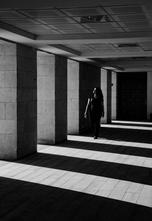 Free A woman walks through a shadowy colonnade in Ankara, Türkiye, casting dramatic shadows. Stock Photo