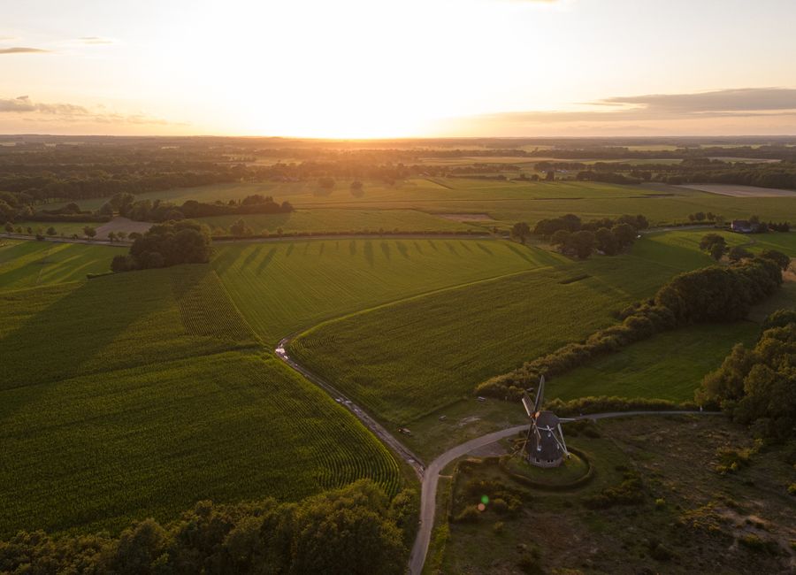 A mesmerizing aerial photo capturing the lush green fields and a windmill in the Dutch countryside at sunset.