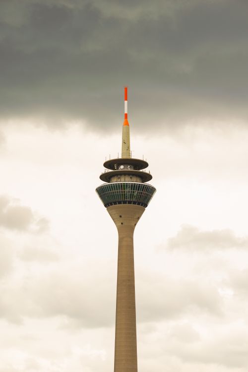 Free View of the iconic Rheinturm Tower in Düsseldorf, Germany, beneath a cloudy sky. Stock Photo