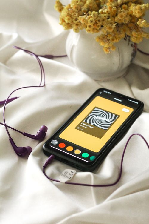 Free Smartphone with purple earbuds and yellow flowers creates a tech-inspired still life scene. Stock Photo