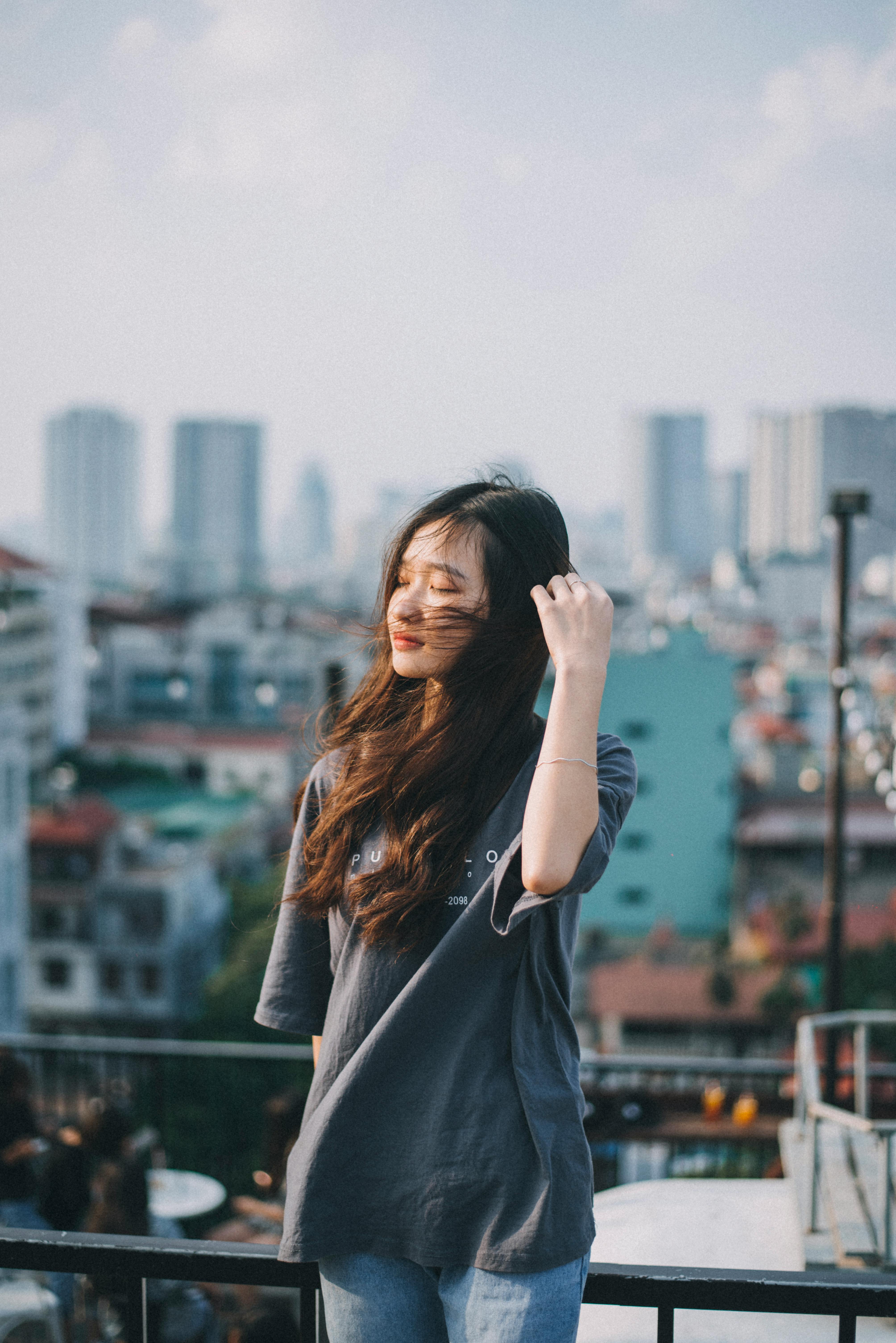 A young woman with long hair stands on a rooftop in Hanoi, basking in the urban view.
