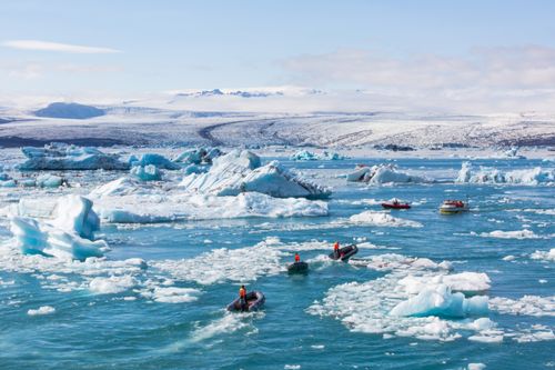 Free A striking view of icebergs in a cold ocean with inflatable boats navigating the icy waters. Stock Photo