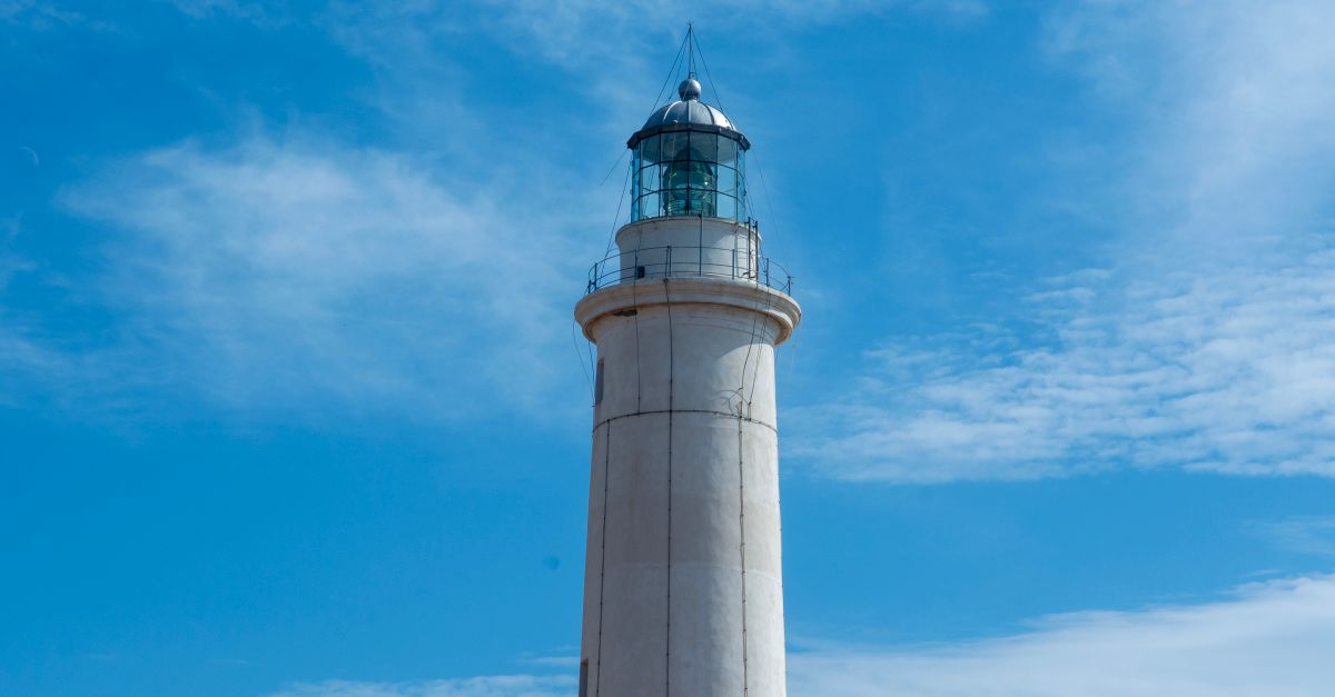 A stunning lighthouse stands tall against a vibrant blue sky in Sicily, Italy.