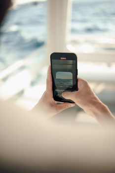 A man takes a photo of the sea with a smartphone on a cruise ship.