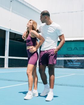 Athletic couple in sportswear posing confidently on a sunny tennis court.