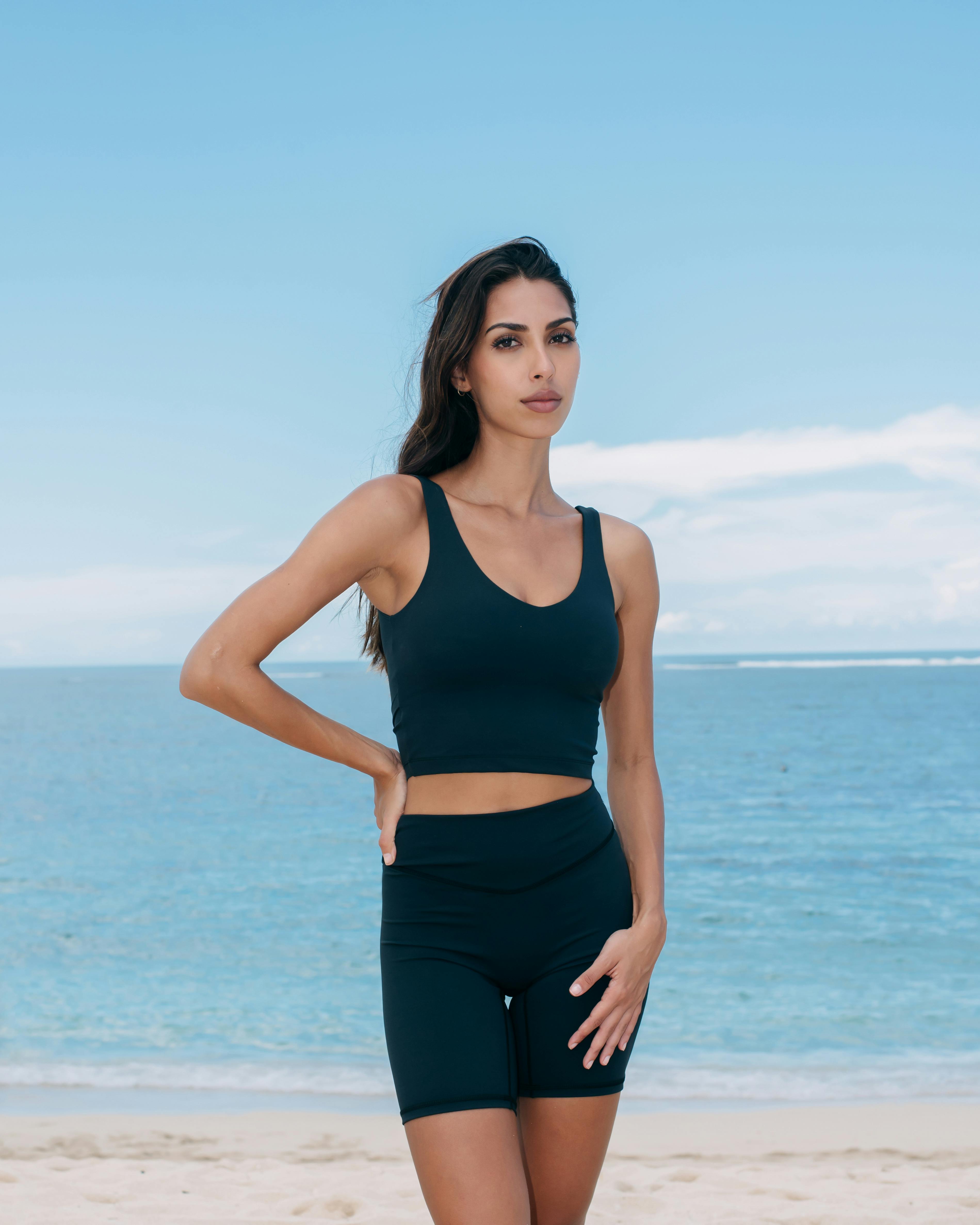 A woman in black sports bra and shorts on the beach · Free Stock Photo