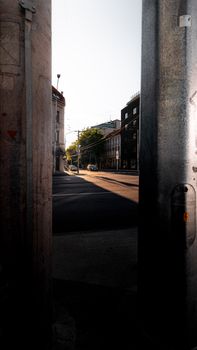 A city street view at sunrise, framed by industrial metal bars, highlighting early morning shadows.
