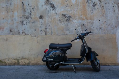 Free A classic Vespa scooter parked against a weathered and textured urban wall. Stock Photo
