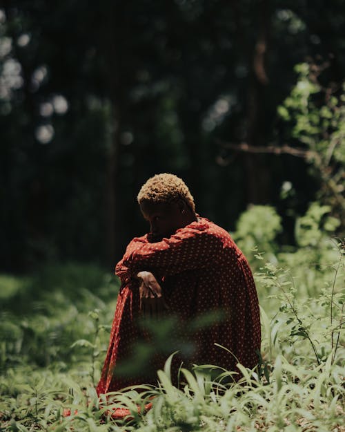 Photo of a Woman Wearing a Red Dress Sitting in a Forest Glade