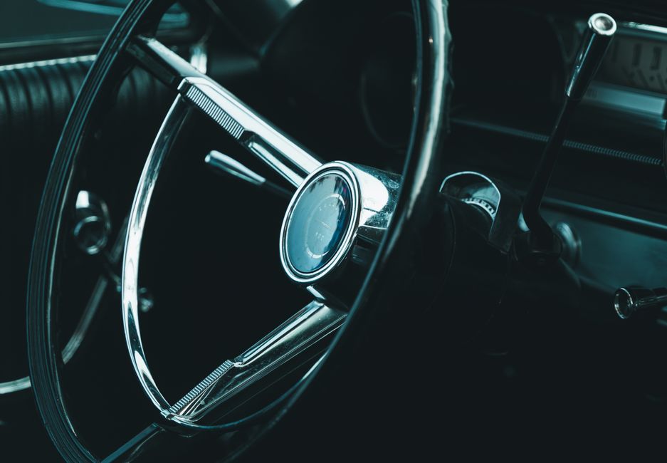 Close-up of a classic car's steering wheel showcasing retro design and chrome detailing.