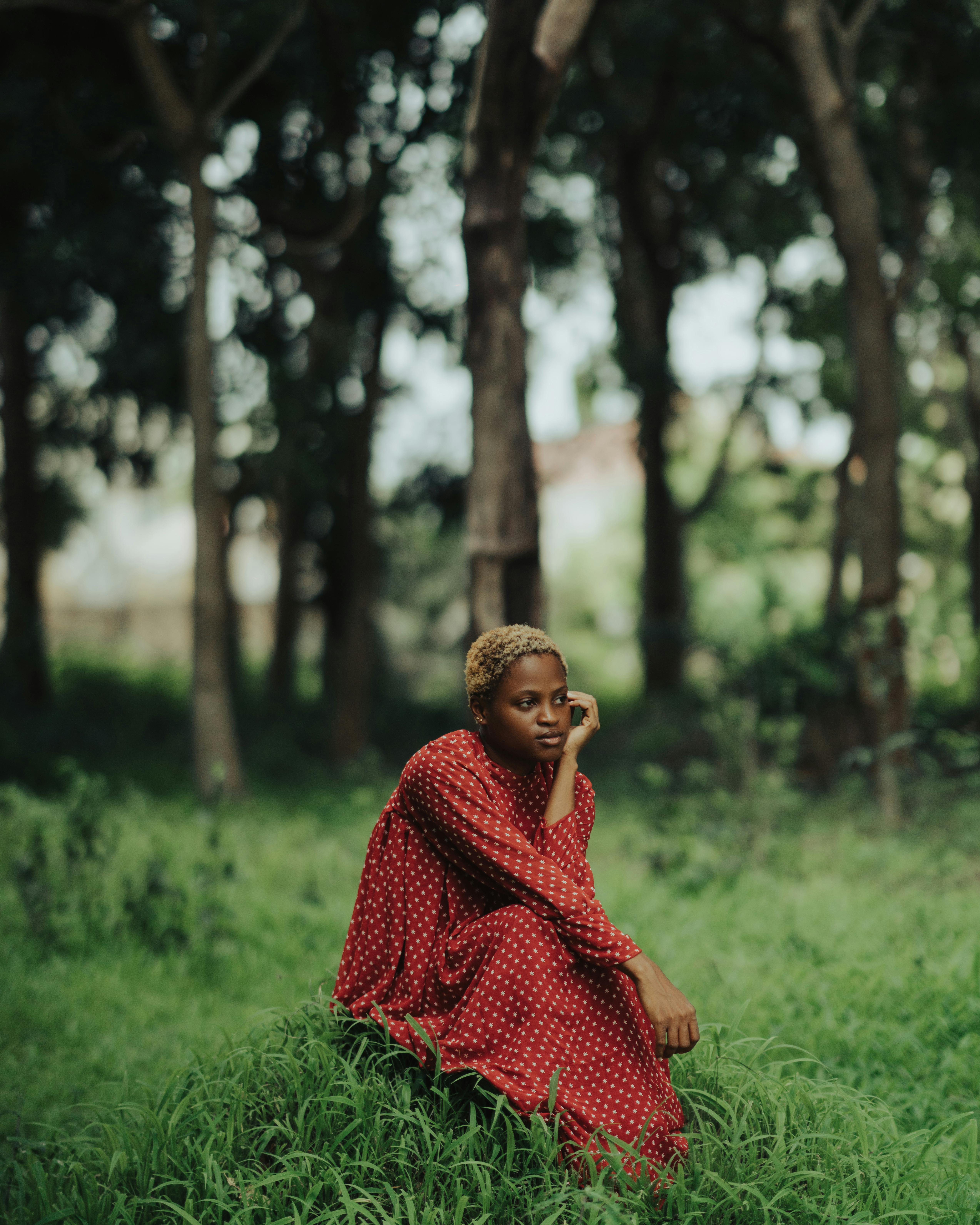 Black woman in a red dress sitting in a lush green forest in Ilorin, Nigeria.