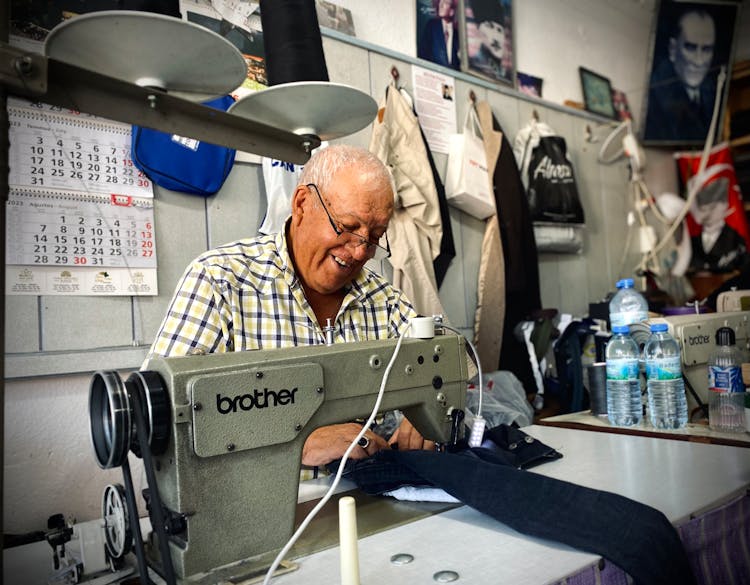 Senior Man Fixing Jeans With A Sewing Machine