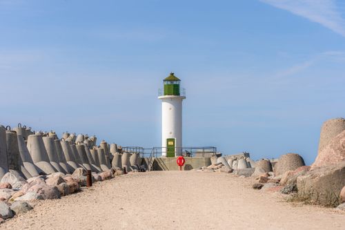 Free White lighthouse along a rocky breakwater path on the Baltic Sea under clear skies. Stock Photo