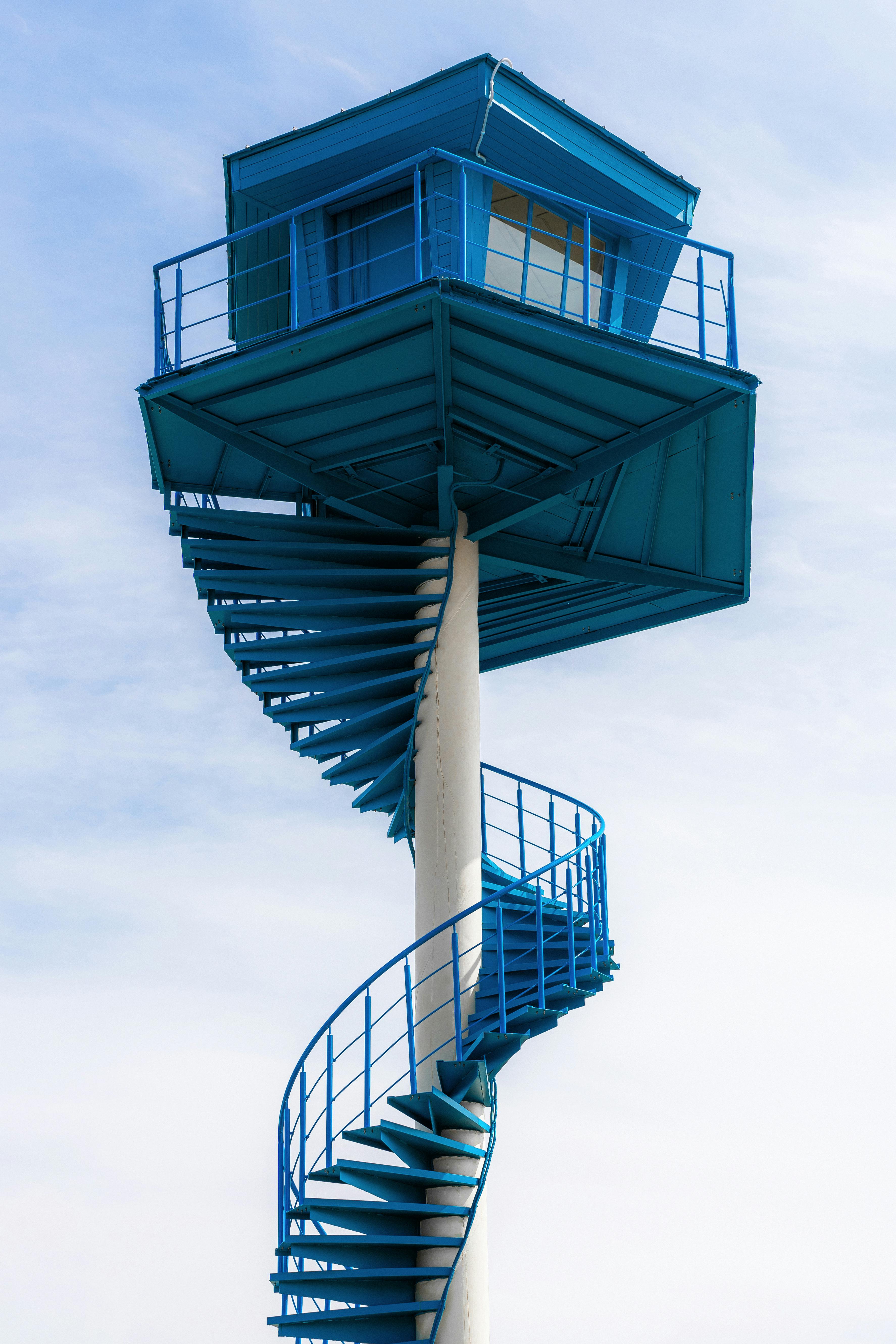 A striking blue lifeguard tower with unique spiral stairs under a clear sky in Ventspils, Latvia.