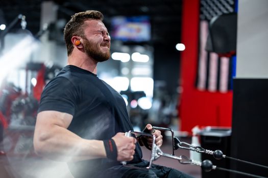 A muscular man in a gym performs an intense workout, emphasizing strength and focus.