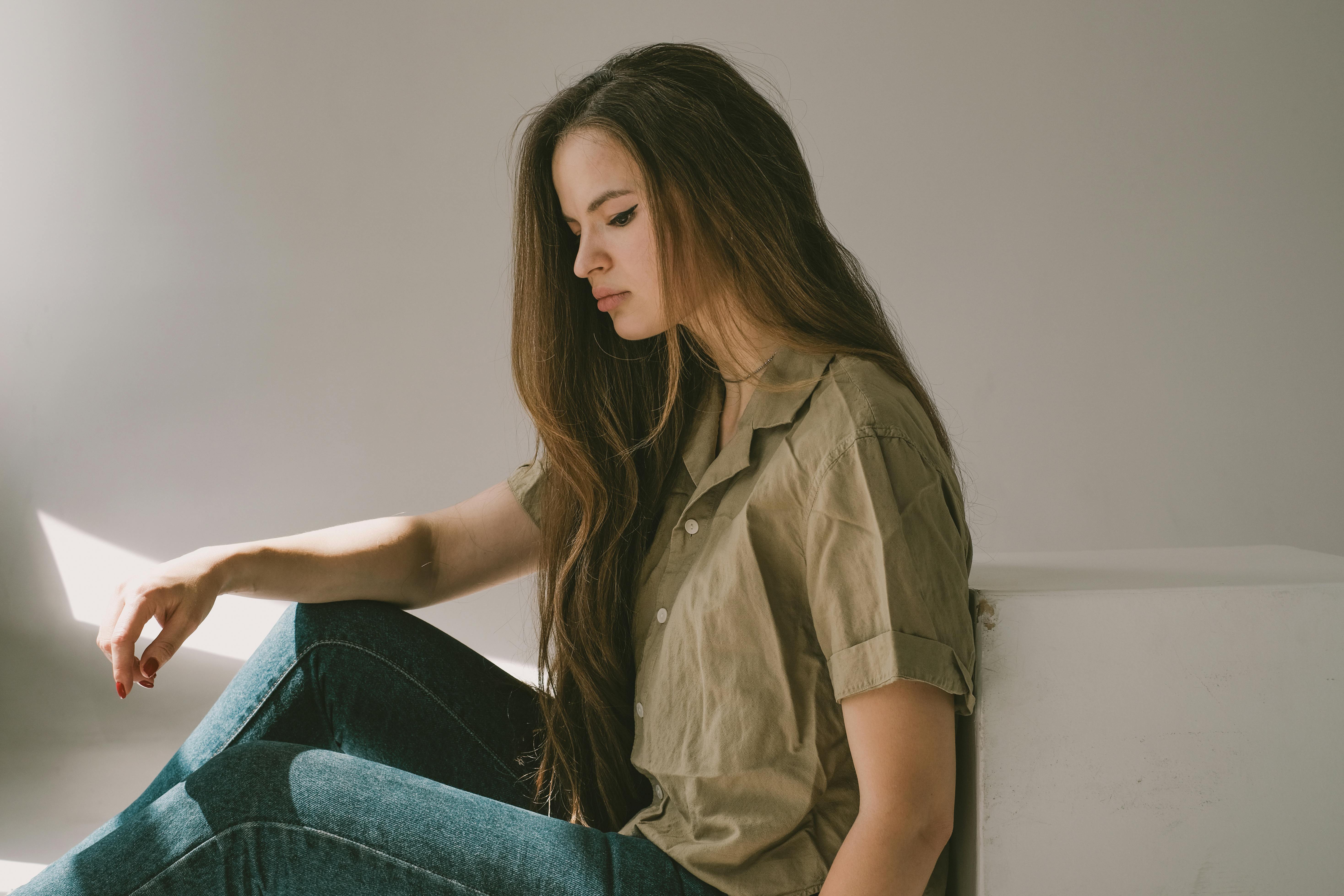 a sad girl with long hair sitting on a floor thinking