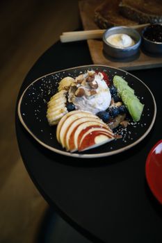 A delightful fruit dessert featuring ice cream, nuts, and fresh fruit slices on a stylish black plate.
