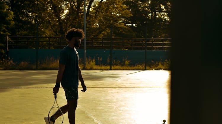 Man Walking On Sunlit Tennis Court