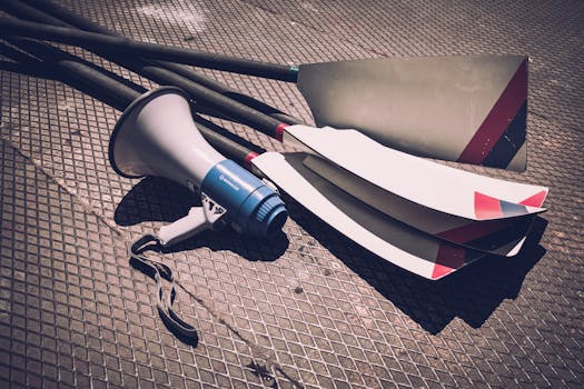 Close-up of a megaphone and rowing oars lying on a sunlit metal ground, showcasing sports gear.
