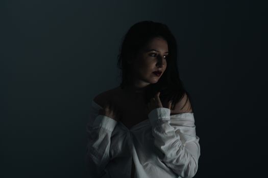 Dramatic portrait of a woman with dark lighting and a white shirt.