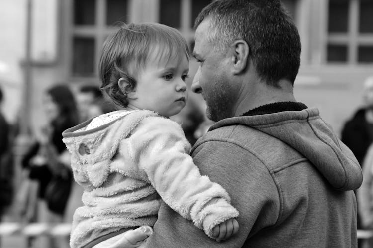 Black And White Candid Shot Of A Father Holding His Little Daughter Outside In City