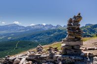 Stacked stones forming a cairn with a stunning view of a mountain range under a clear blue sky.