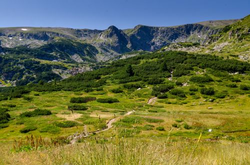 Free Explore the serene beauty of a lush green valley surrounded by towering mountains under a clear summer sky. Stock Photo