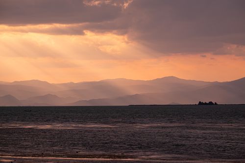 Free Breathtaking sunset over the sea with dramatic sunbeams illuminating the distant hills. Stock Photo