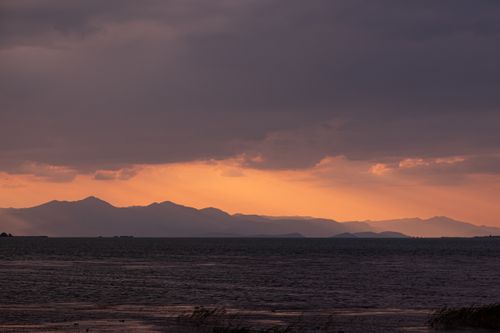 Free Tranquil scene of a sunset behind mountains over a calm sea, perfect for nature themes. Stock Photo